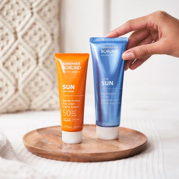 ANNEMARIE BÖRLIND SUN Sonnencreme LSF 50 und After Sun Lotion auf Holztablett, Hand hält Lotion